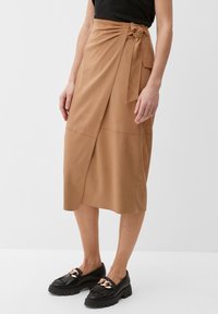 Jupe en faux cuir marron avec une détail de nœud à la taille, présentant une texture lisse et un ourlet asymétrique.