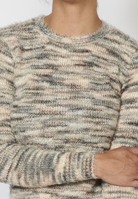 Stickad tröja med en fluffig textur i beige, grå och persikofärgade ränder, med rund halsringning och långa ärmar.