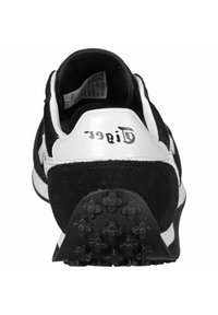 Svart och vit sneaker med ovandel i mocka och mesh, vadderad krage och strukturerad sula med multidirektionella nubb för grepp.