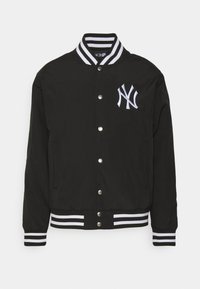 Chaqueta varsity negra con logo de NY bordado en blanco, cierre de botones a presión, cuello y puños de canalé a rayas, y bolsillos laterales.