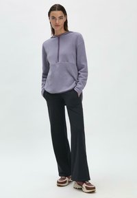 Lila Fleece-Pullover mit einem halben Reißverschluss, kombiniert mit schwarzen weiten Hosen und braunen sowie rosa Sneakers. Glatte Textur, lockere Passform.
