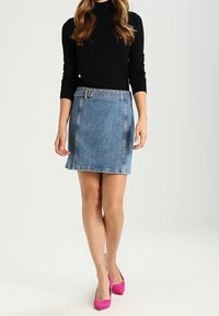 Gonna mini in denim con un lavaggio azzurro chiaro, dotata di una fibbia frontale, abbinata a un top nero a maniche lunghe e tacchi rosa.