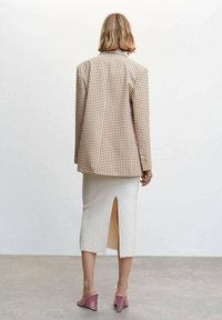 Blazer pied-de-poule marron et crème, jupe en maille crème avec fente arrière, et mules roses, vus de dos. Textures lisses et silhouette ajustée.