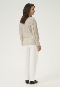 Beige pletený svetr s diamantovým vzorem, balónovými rukávy a rovný střih, kombinovaný s bílými kalhotami rovného střihu a černými balerínami.