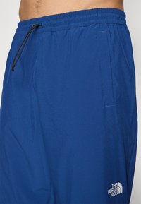 Μπλε ελαφρύ σορτσάκι με ελαστική μέση, λεπτομέρεια κορδονιού, πλαϊνή τσέπη και λευκό λογότυπο στο κάτω μέρος. Λείος υφασμάτινος σχεδιασμός.