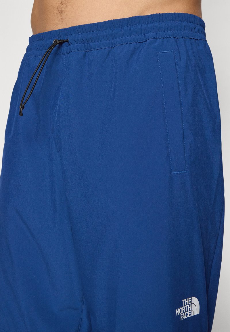 Blaue leichte Shorts mit einem elastischen Bund, Kordelzug, Seitentasche und einem weißen Logo am unteren Saum. Angenehme, glatte Textur.