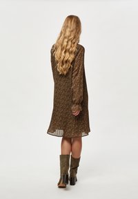 Ruskea kukallinen mekko, jossa on pleatattu muotoilu ja pitkät hihat, yhdistettynä oliivinvihreisiin korkokenkiin. Silkkinen, teksturoitu kangas, puolipitkä tyyli.