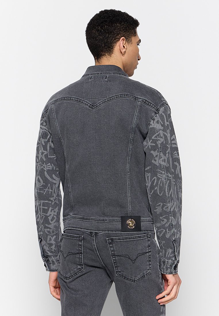 Chaqueta de mezclilla gris con una tela texturizada y detalles impresos en las mangas, cuello tradicional y un parche con logo en la parte posterior.