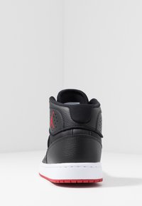 Zapatilla alta con parte superior de cuero negra, acentos rojos, cuello acolchado y mediopie blanco con suela roja. Logo de Air Jordan en el talón.