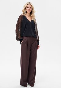 Czarna bluzka z przezroczystymi, wzorzystymi rękawami; brązowe szerokie spodnie. Miękki materiał, luźny krój, dekolt w kształcie litery V oraz boczne kieszenie w spodniach.