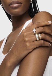 Tres anillos exhibidos en los dedos: un anillo ovalado de plata; un aro de oro; y un anillo con gema que tiene una piedra rosa y pequeños acentos azules.