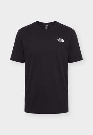 Мъж, носещ черна тениска с бяла графика на скиор и лого "The North Face" на гърба, стои с гръб към камерата.