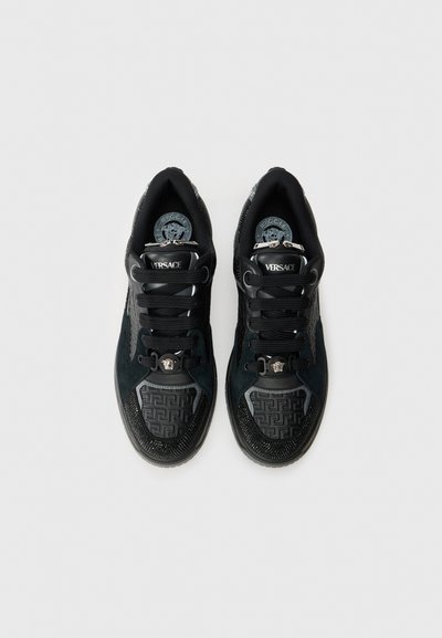 Black sneakers featuring a mix of suede and textured materials, with a patterned toe cap, lace fastenings, and bold logo accents.