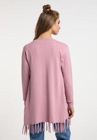 Cardigan rosa a maniche lunghe con vestibilità rilassata, caratterizzato da un orlo frangiato e una consistenza morbida, abbinato a jeans azzurri chiari.