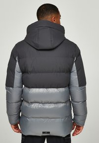 Grijze en zwarte pufferjack met een capuchon, met doorgestikte secties en een gladde textuur. Het ontwerp bevat contrasterende kleurvlakken.
