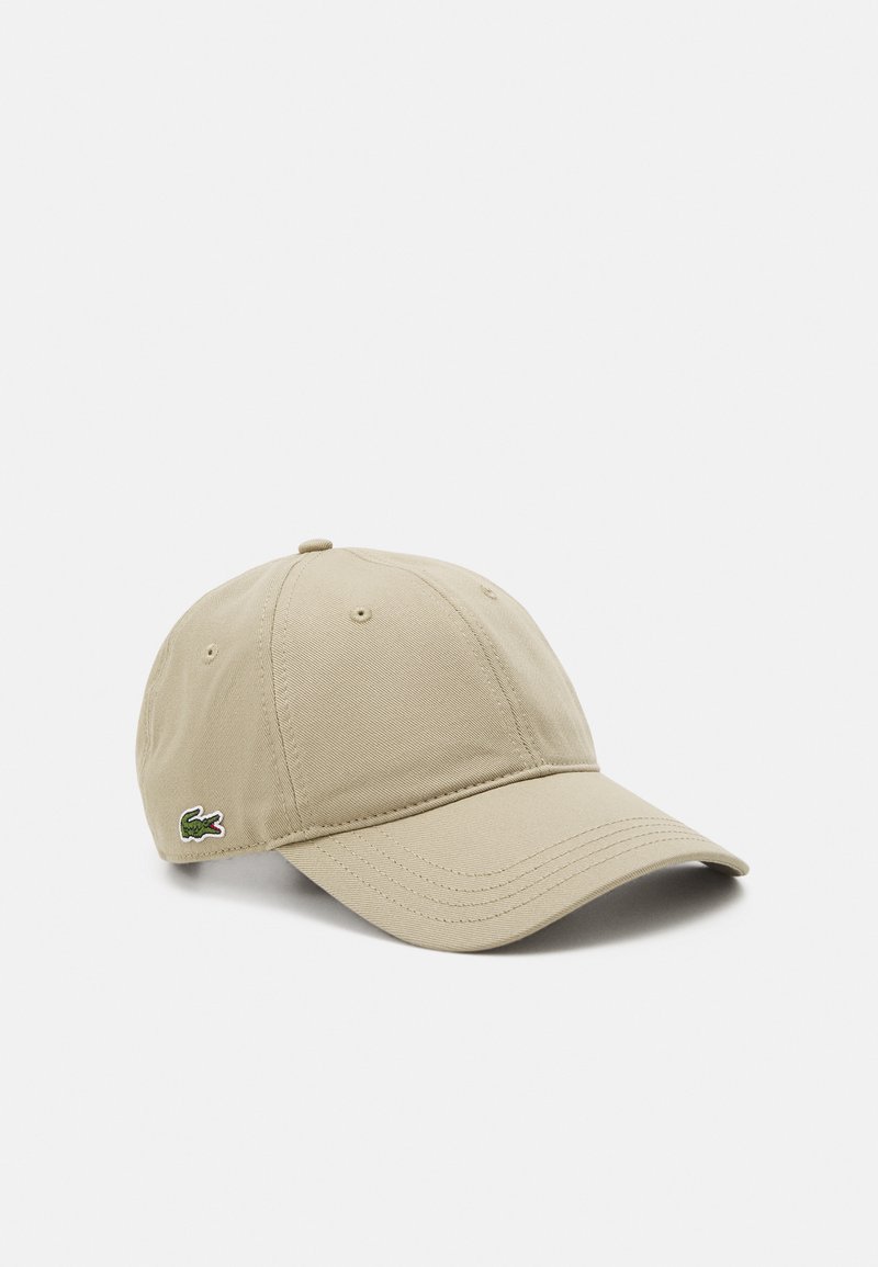 Beige bomullcaps med buet skygge, seks paneler, og en grønn brodert krokodille-logo på venstre side. Teksturert stoff og sydd detaljer.