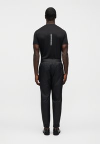 Μαύρο κοντομάνικο πουκάμισο με κάθετη ανακλαστική ρίγα στην πλάτη, σε συνδυασμό με μαύρο, υφασμάτινο αθλητικό παντελόνι και μαύρα παπούτσια.