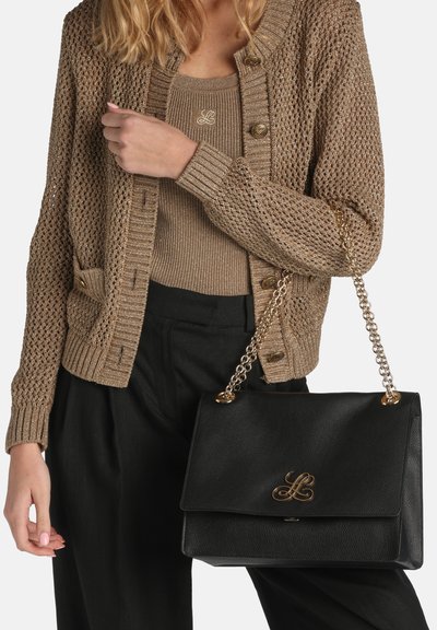 Black leather handbag with a gold logo, featuring a chain strap. Styled with a beige knit cardigan and top, with black loose pants.