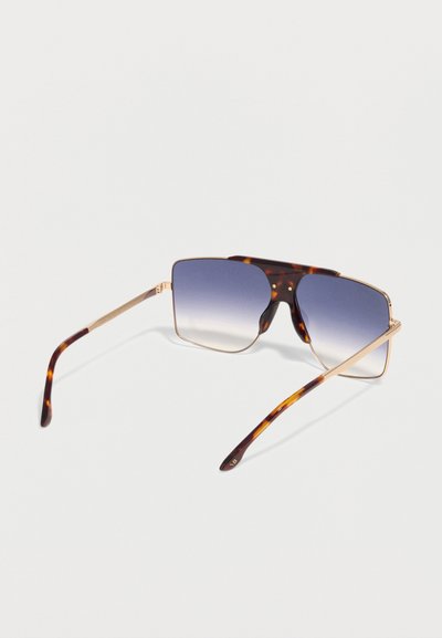 Γυαλιά ηλίου με σκελετό από χελώνα, ορθογώνιους φακούς μπλε ανοιχτής απόχρωσης και λεπτούς χρυσούς μεταλλικούς βραχίονες πάνω σε λευκή επιφάνεια.