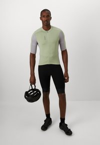 Kurzärmeliges Radtrikot in Hellgrün mit grauen Akzenten, mit Frontreißverschluss, kombiniert mit schwarzen Radshorts und einem schwarzen Helm.