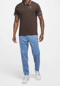 Brun polo skjorta med vit randig krage, kombinerad med ljusblå idrottsbyxor. Vita sneakers fulländar looken.