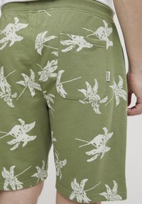 Pantaloni corti verdi in cotone con un motivo a foglia tropicale bianca, dotati di tasca posteriore e cintura elastica per il massimo comfort.
