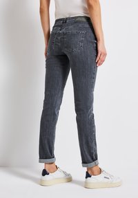 Mörkgrå jeans med rak passform, med fem fickor, uppvikta fållar och denimstruktur. Bärs med vita sneakers och en åtsittande topp.