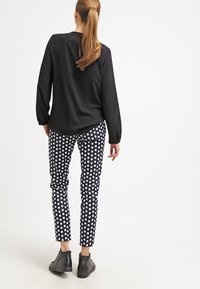 Blusa nera a maniche lunghe abbinata a pantaloni a scacchi blu navy, con una vestibilità slim e scarpe nere, vista dal retro.