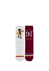 Calzini bianchi e bordeaux con design: un lato presenta "FREE DOBBY" e una silhouette di un elfo, l'altro "PLATFORM 9¾" e "HOGWARTS EXPRESS."