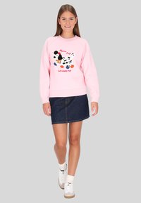 Sudadera rosa con un gráfico de perro y texto en el frente, combinada con una falda vaquera oscura y zapatillas blancas, mostrando un estilo casual.