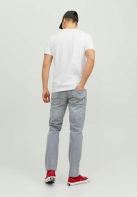 T-shirt blanc à manches courtes, jeans gris clair et baskets rouges. Personne vue de dos, portant une casquette noire. Design simple, sans motifs.