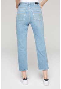 Los pantalones vaqueros de denim azul claro presentan un corte recto, bolsillos traseros con acentos de costura dorada y se llevan con zapatillas blancas.