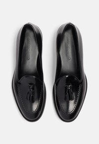 Schwarze Lackleder-Loafer mit runder Spitze, dekorativen Quasten und tonalen Nähten. Glatte Textur und praktische Slip-On-Design.