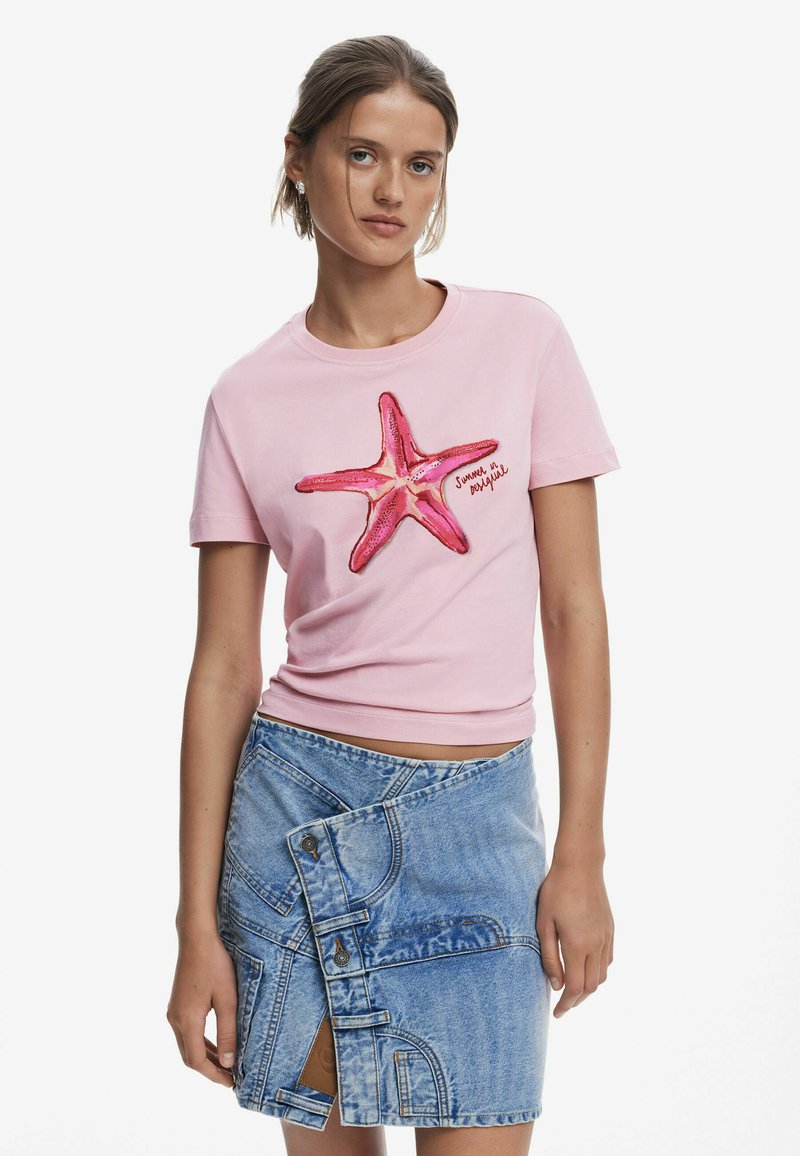 Pink cotton t-shirt featuring a large embroidered starfish design in shades of pink. Paired with a light blue denim wrap skirt with button details.