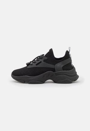 Czarny sportowy sneaker z grubą teksturowaną podeszwą, siateczkową cholewką, sznurowaniem z przodu i pętlą na pięcie na jednolitym tle.
