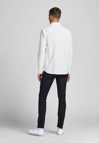 Hvit langermet skjorte med knapp-ned krage, brukt sammen med mørke slim-fit jeans og hvite sneakers, har et teksturert stoff og en tettsittende design.