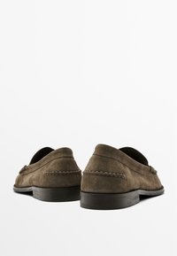 Mocassins en daim marron à profil bas, dotés d'une couture décorative sur le dessus et d'une semelle en caoutchouc texturée. Fini lisse.