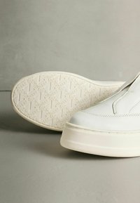 Pantofi slip-on albi, din piele texturată, cu vârf rotund și talpă groasă din cauciuc crem cu model în relief.