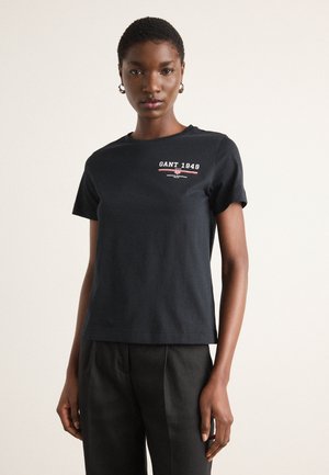 T-shirt en coton noir à manches courtes, avec un logo rouge et blanc "GANT 1949" sur la poitrine. Design à coupe droite.