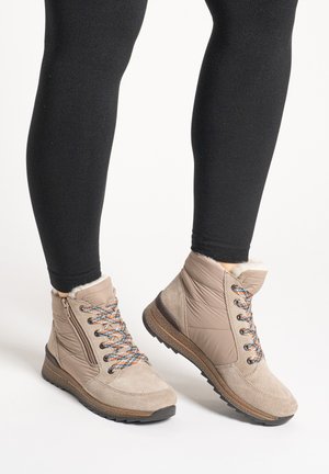 Bottes d'hiver beige à la cheville avec des lacets colorés, des fermetures éclair latérales et une doublure en fourrure, portées avec des leggings noirs sur un fond neutre.