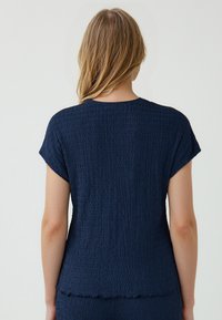 Dunkelblaues Kurzarmoberteil aus strukturiertem, zerknittertem Material. Verfügt über einen runden Ausschnitt und einen leicht gewellten Saum.