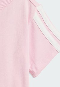 Camiseta rosa de manga corta con cuello acanalado y rayas blancas a lo largo de los hombros. Tejido de algodón suave con textura lisa.