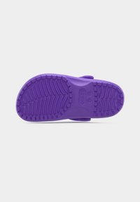 Σόλα μοβ παντόφλας Crocs με σχεδιασμένο πέλμα και σημαίες μεγέθους σε απλό λευκό φόντο.