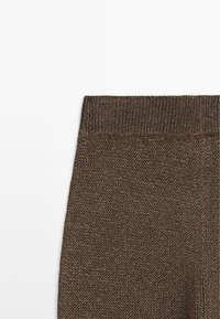 Detailní záběr hnědé pletené látky s žebrovaným elastickým pasem, pravděpodobně součást oblečení jako kalhoty nebo sukně.