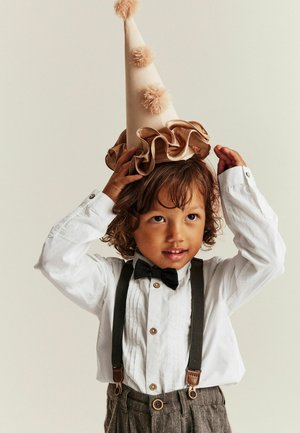 Barn iført en hvid skjorte med knapper, butterfly, grå stribede bukser og en beige festhat med flæser og pomponer.