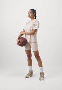 Šviesiai rožinė trumpomis rankovėmis marškinėliai ir derančios dviratininkų šortai, su pilkais sportiniais bateliais ir baltais kojinaitėmis, laikančiais krepšinį. Paprastas, prigludęs dizainas.