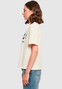 Kortærmet cremefarvet bomulds t-shirt med grafisk tryk af en grøn og rød nisse samt tekst på forsiden, afslappet pasform, blød tekstur og lige kant.