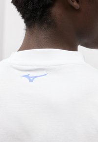 Κοντινό πλάνο του πίσω μέρους του λαιμού ενός ατόμου και του λευκού γιακανού του πουκάμισου με ένα μικρό μπλε λογότυπο αθλητικού ρουχισμού στο πάνω πίσω μέρος.