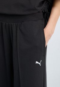 Svarte bomullsjoggebukser med elastisk midje, med en hvit Puma-logo nederst til venstre. Lommer på sidene gir funksjonalitet.