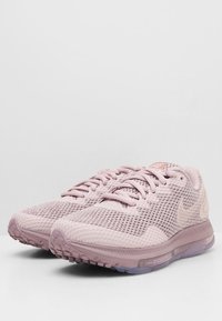Zapatillas de running Nike de color rosa claro con una parte superior de malla transpirable, superficie texturizada y suela acolchada. Presenta un logo visible y un sistema de cordones.